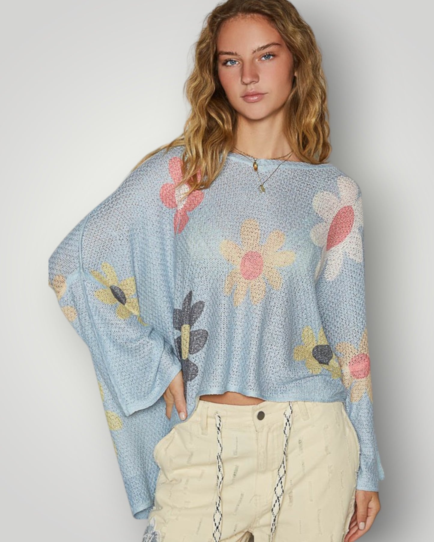 Woman wearing a light blue sweater with floral patterns on a plain background