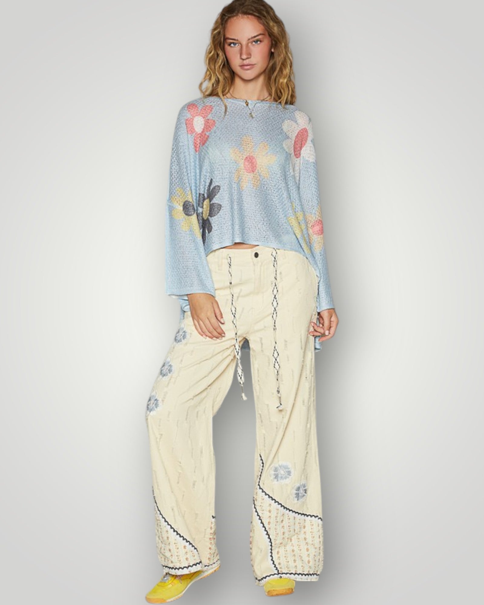 Woman wearing a light blue floral sweater and cream pants on a plain background