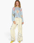 A model wearing a light blue long-sleeve knit top with a colorful floral pattern, paired with cream wide-leg pants featuring blue floral embroidery and drawstrings, and yellow shoes, against a plain white background.
