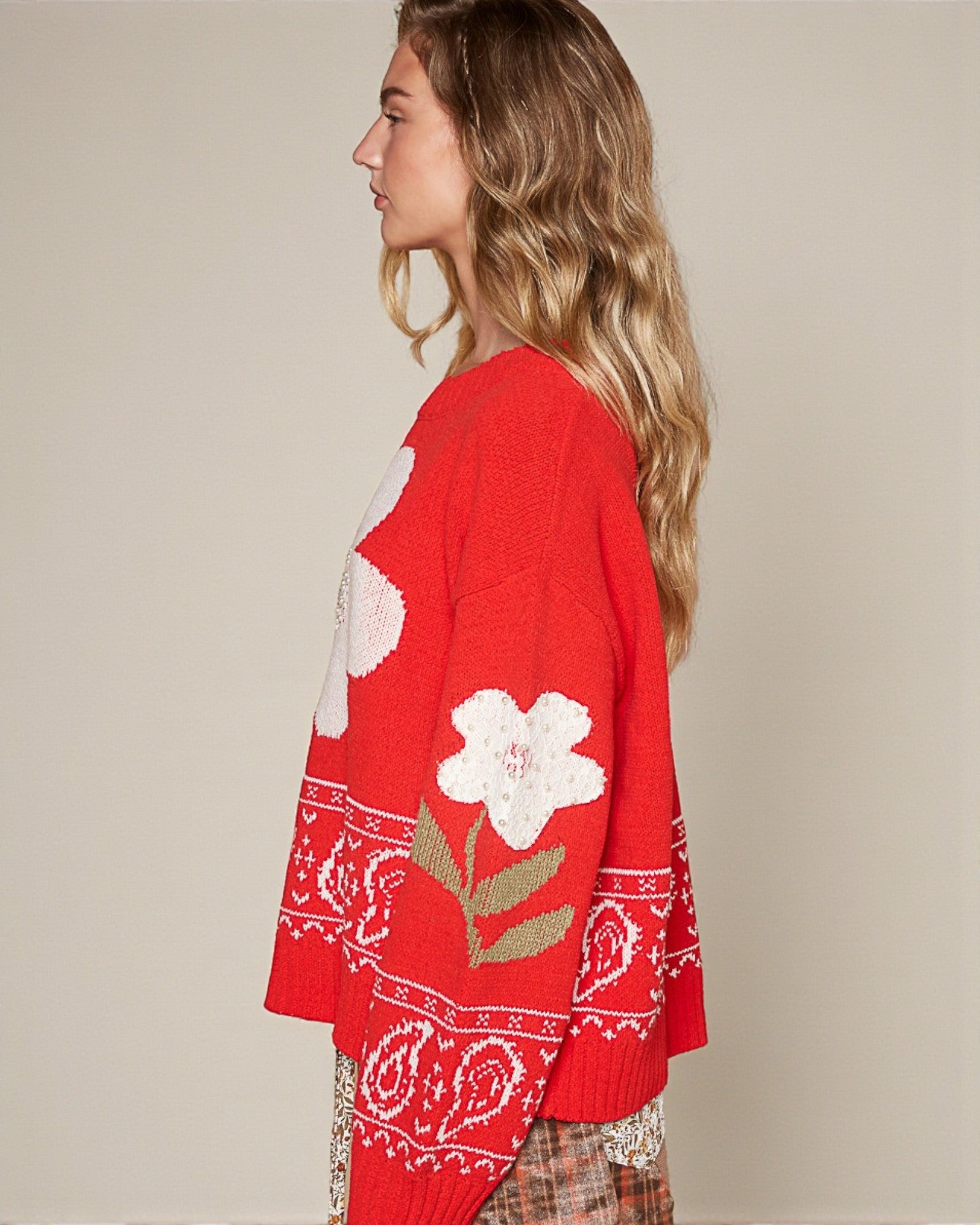 Red sweater with floral patterns worn by a person on a beige background