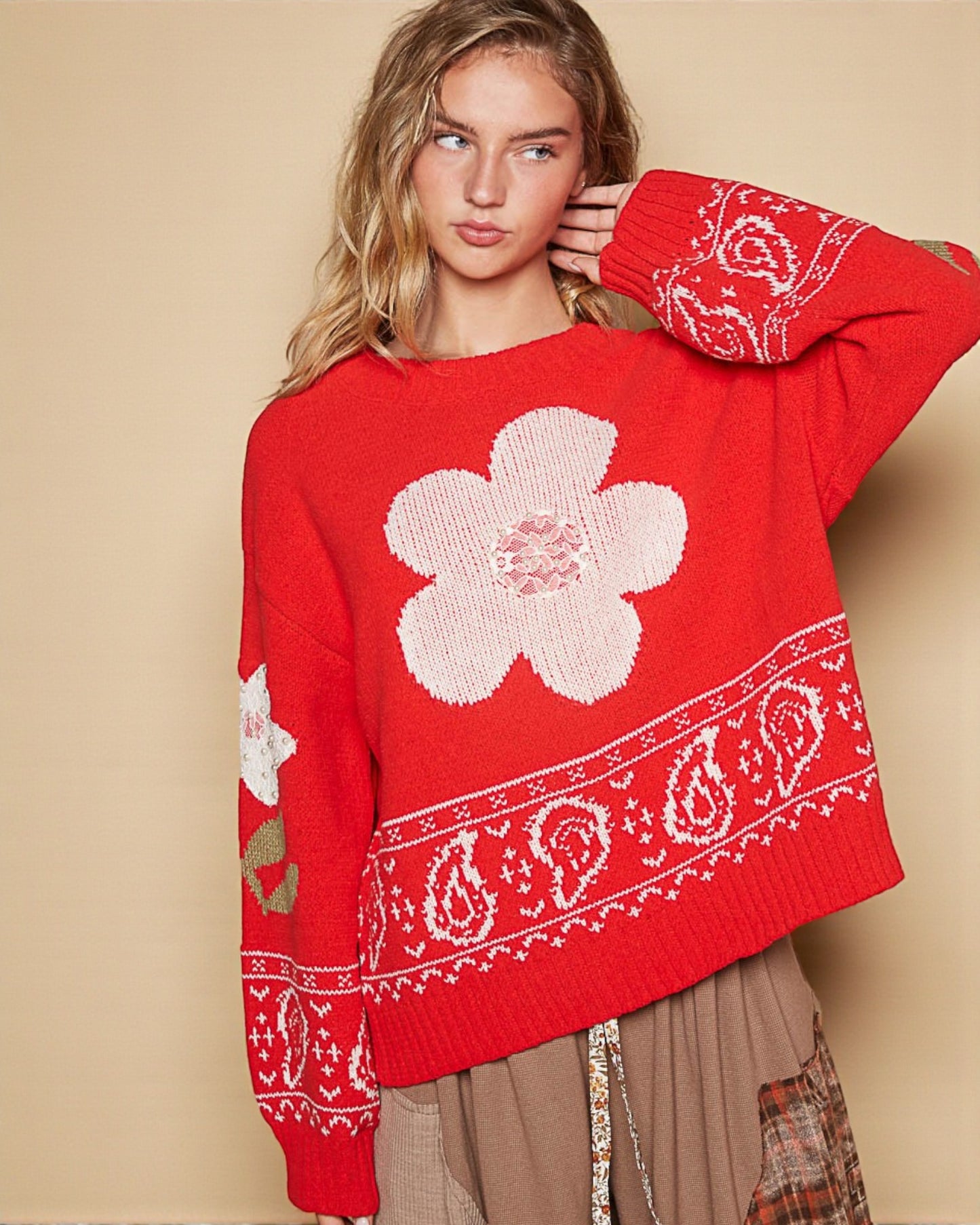 Woman wearing a red sweater with white floral and paisley patterns on a beige background