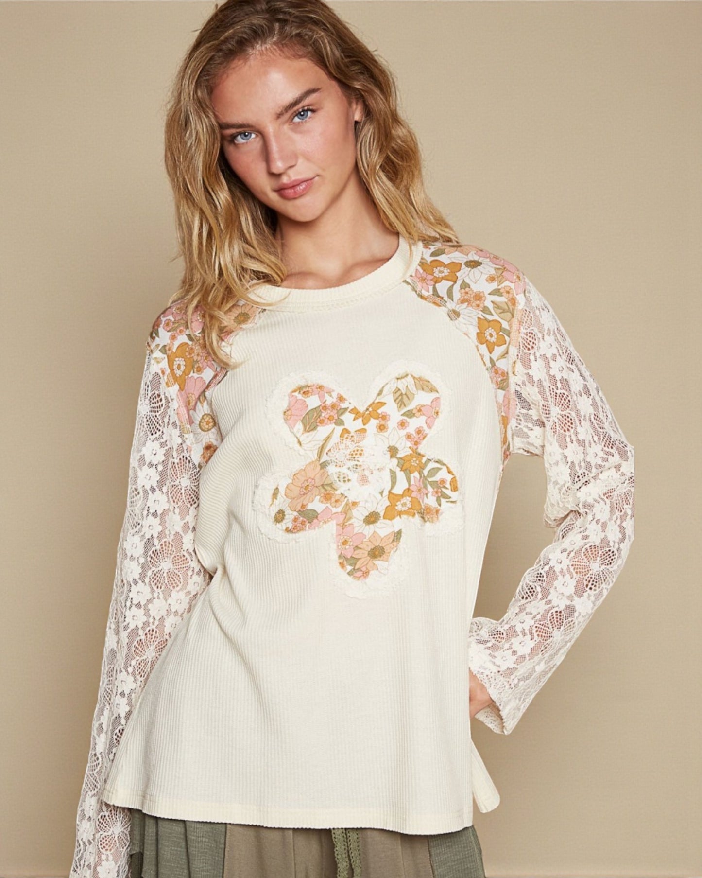 Woman wearing a cream-colored top with floral lace sleeves on a beige background