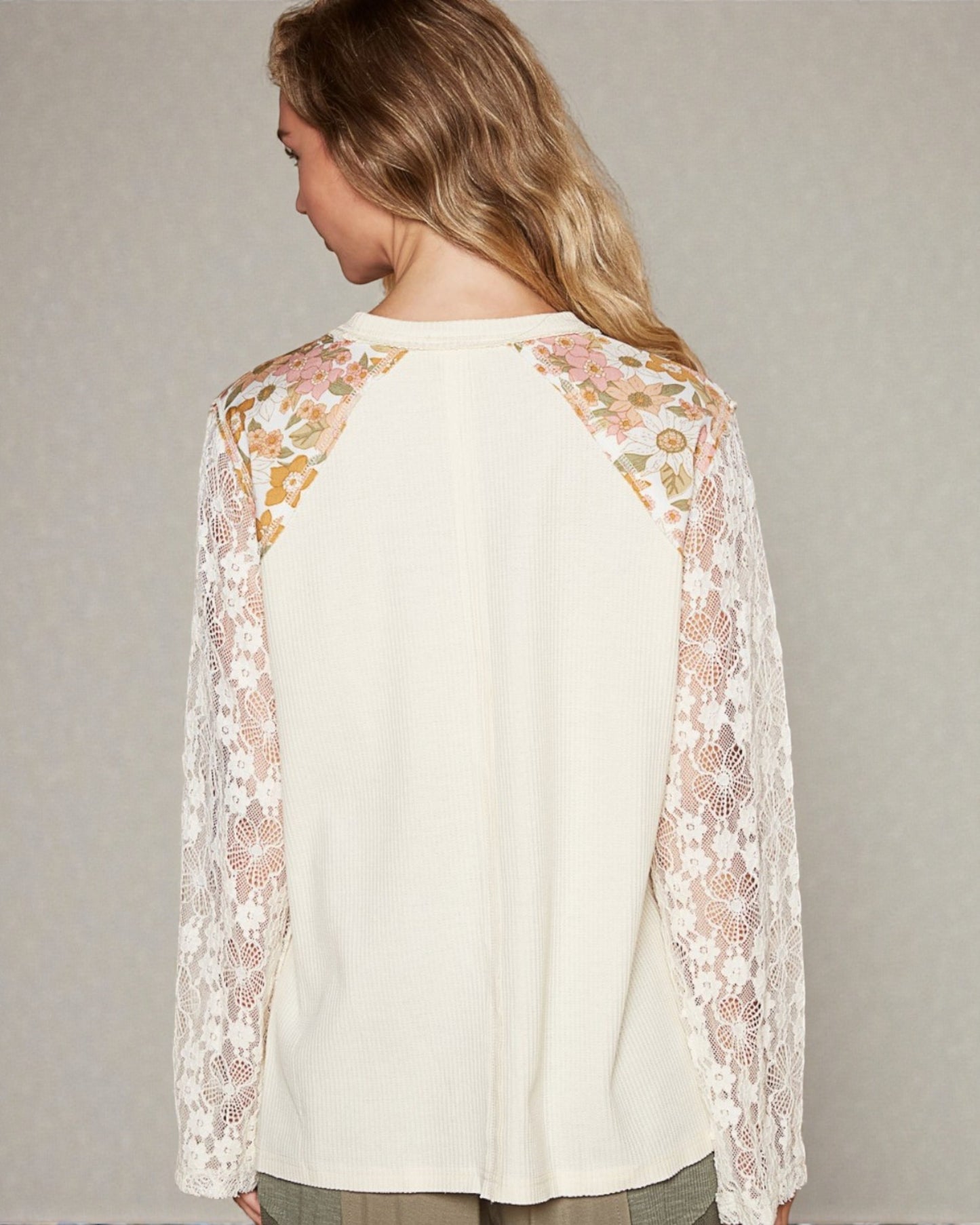 Woman wearing a cream-colored top with floral lace sleeves against a neutral background