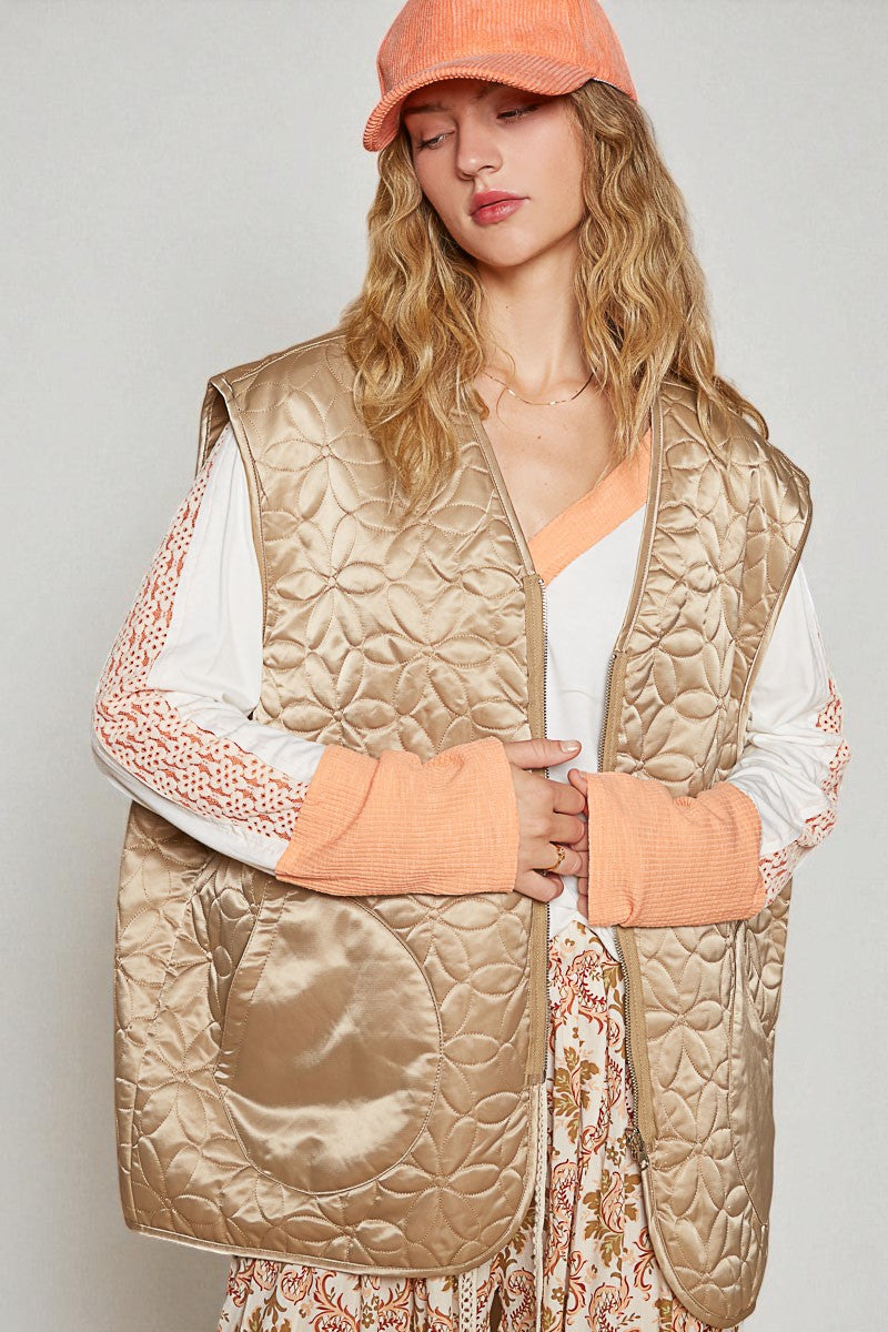 Woman wearing a beige quilted vest over a floral dress with a plain background