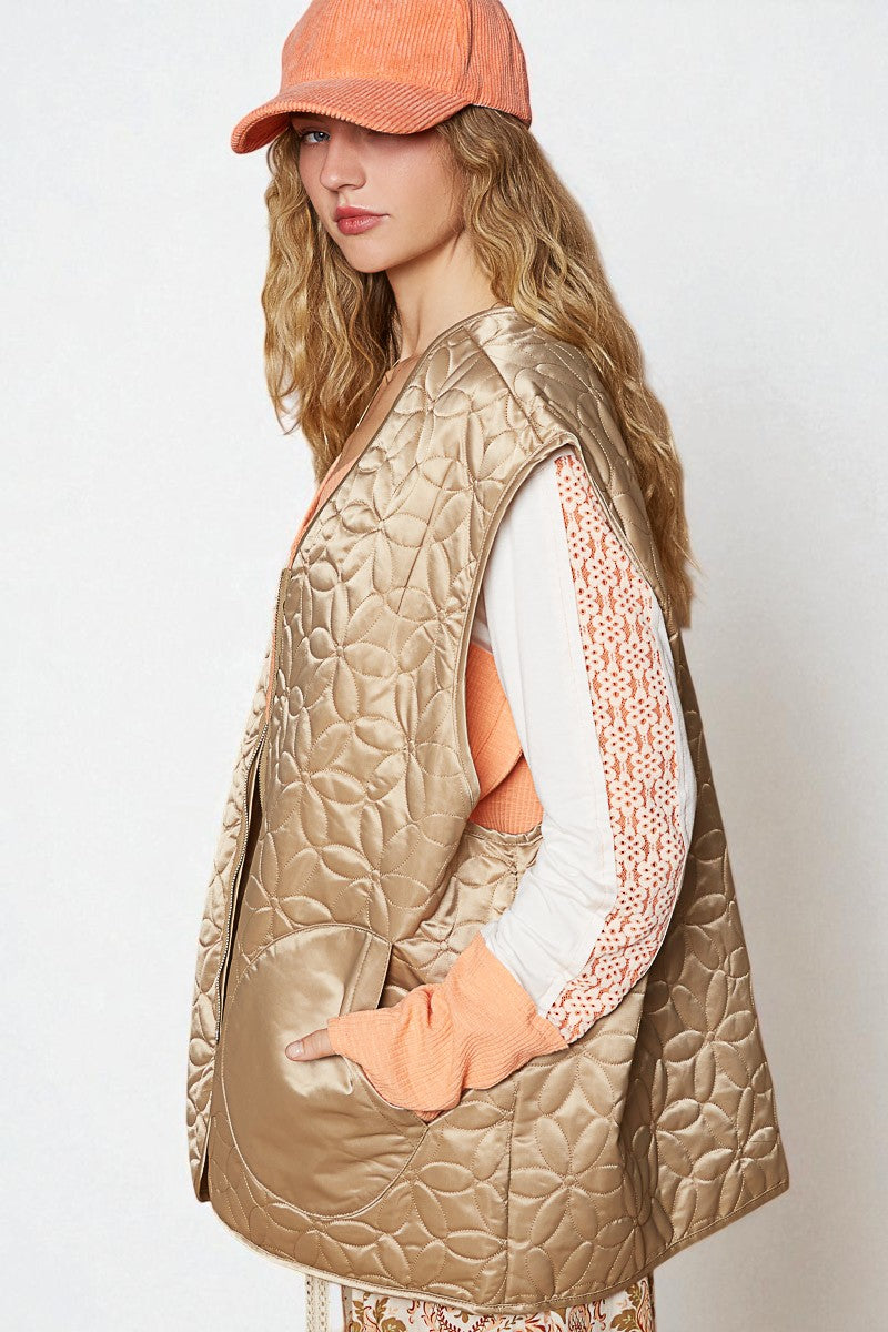 Woman wearing a beige quilted vest and orange cap against a white background