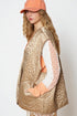 Woman wearing a beige quilted vest and orange cap against a white background