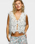 Woman wearing a white lace top with floral pants on a plain background