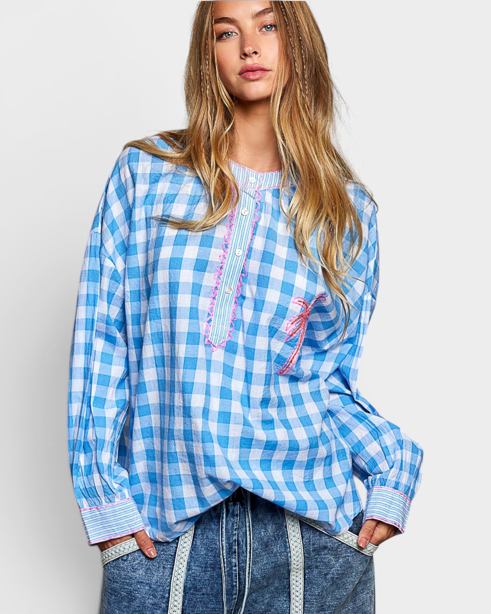Woman wearing a blue and white checkered blouse with decorative elements on a plain background