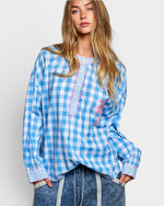 Woman wearing a blue and white checkered blouse with decorative elements on a plain background