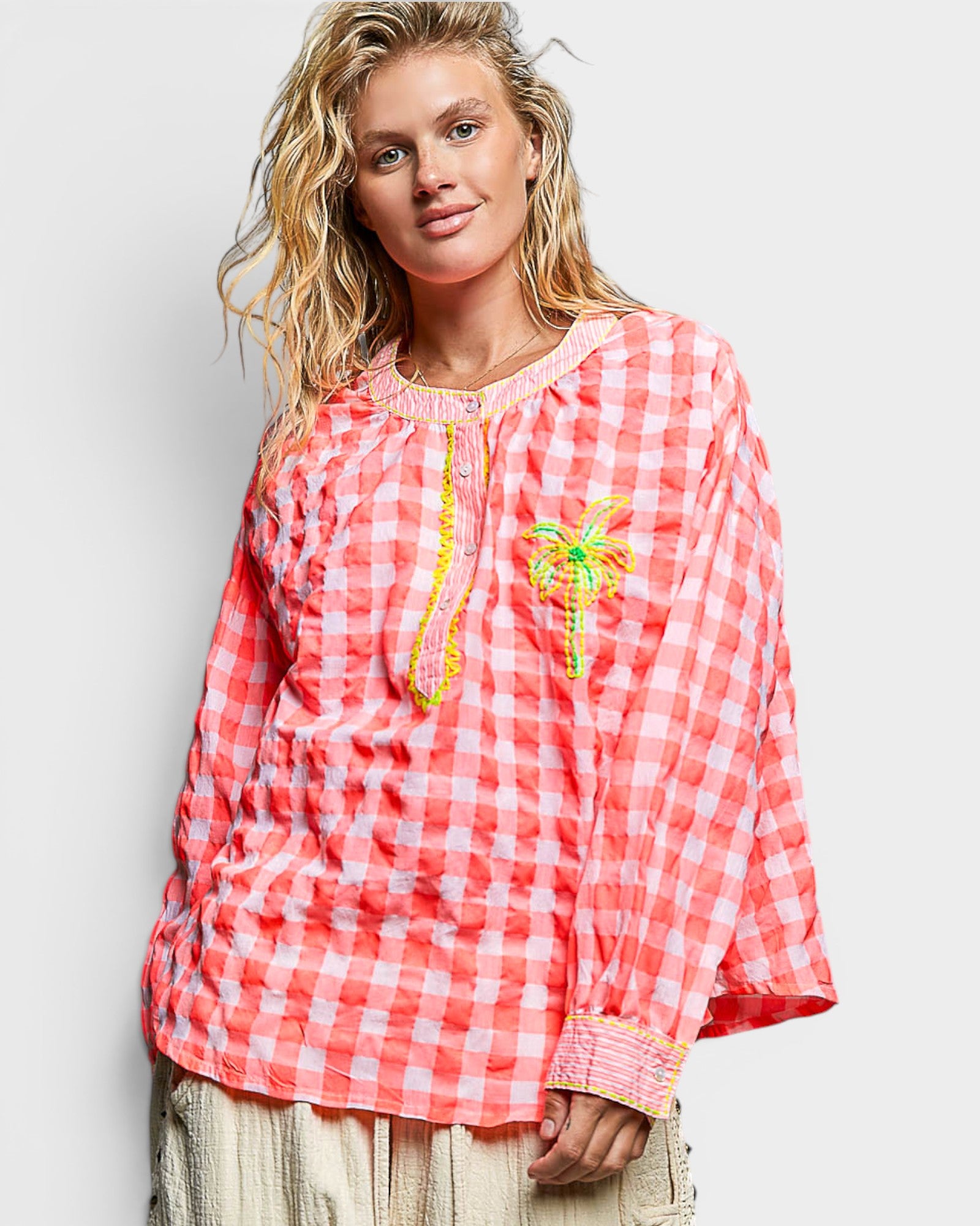 Woman wearing a red and white checkered blouse with palm tree design on a plain background
