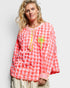 Woman wearing a red and white checkered blouse with palm tree design on a plain background