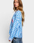 Woman wearing a blue and white checkered shirt with a red logo on a light gray background
