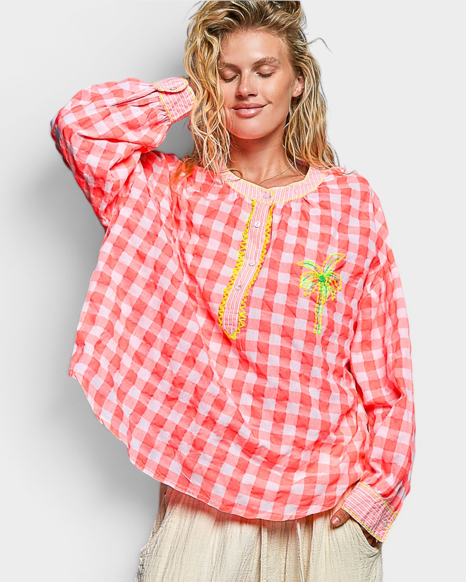 Woman wearing a red and white checkered blouse with palm tree design on a plain background