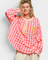 Woman wearing a red and white checkered blouse with palm tree design on a plain background