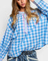 Person wearing a blue and white checkered top with decorative trim on a plain background