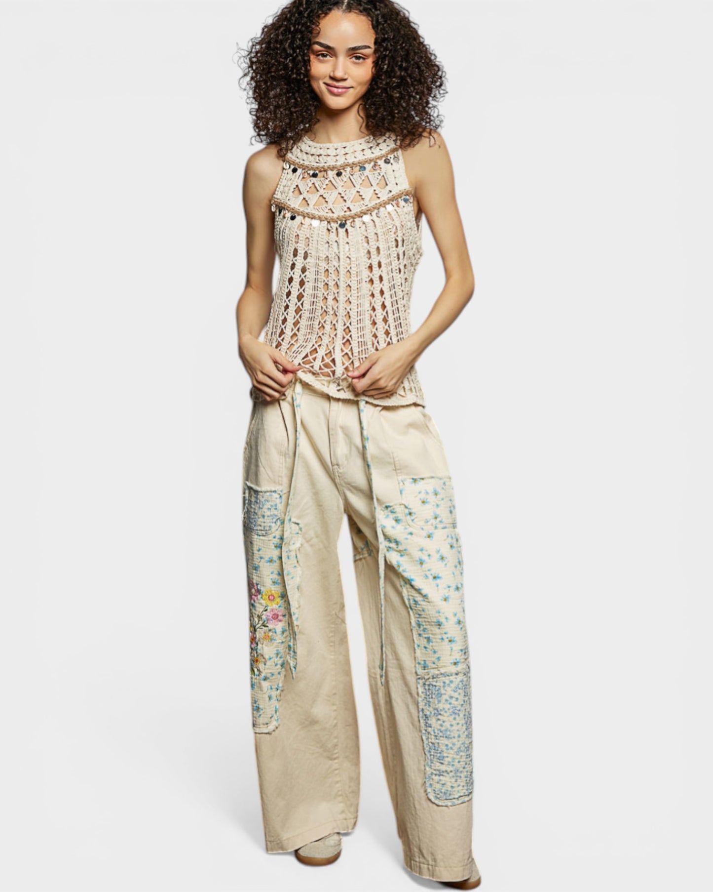 Woman wearing a sleeveless top and wide-leg pants with floral patterns on a white background