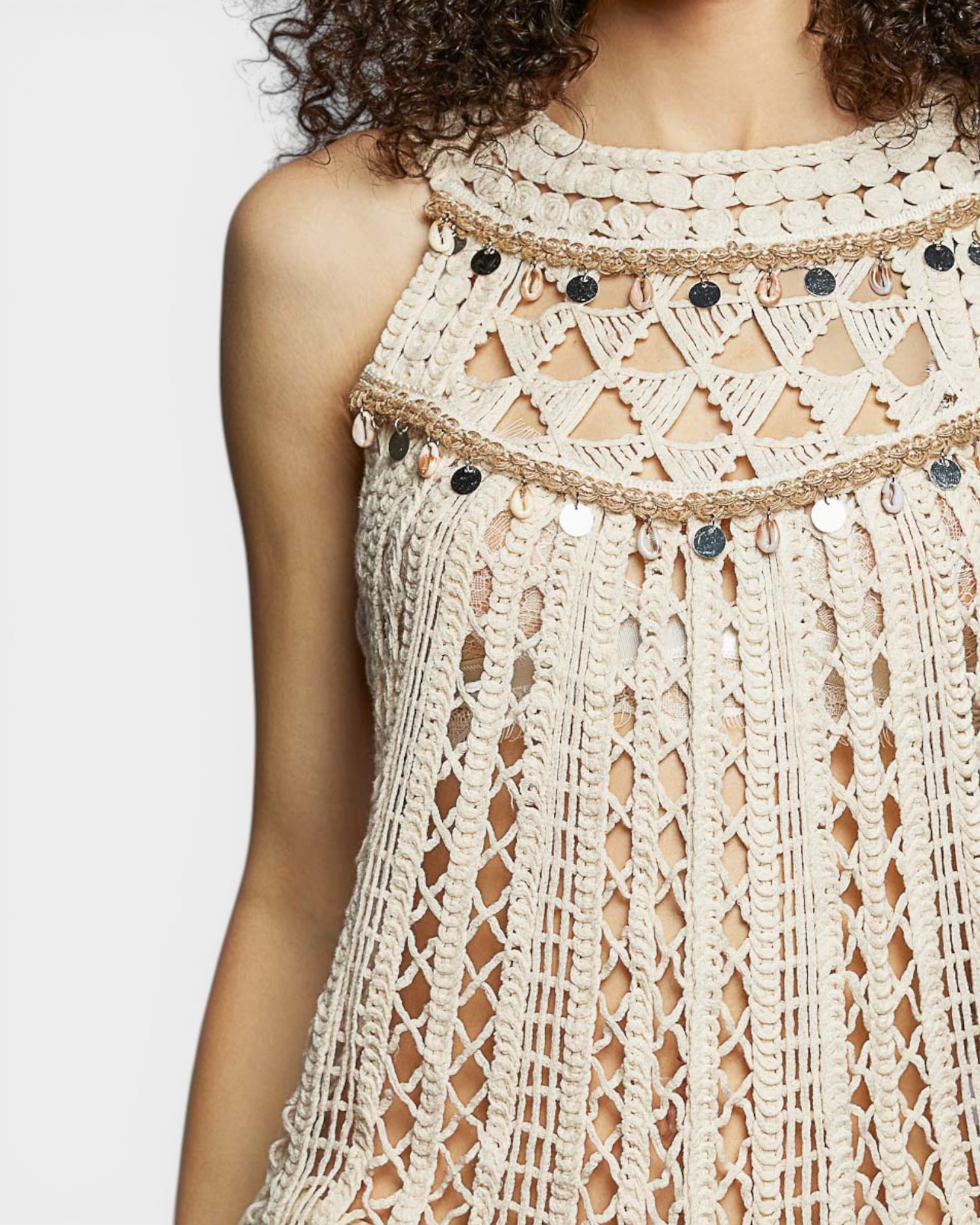 Close-up of a beige crochet dress with black button details on a white background
