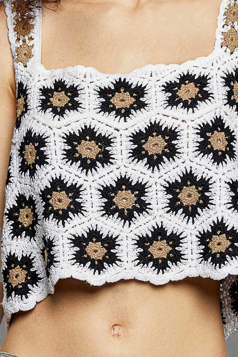 Close-up of a person wearing a white crochet top with black and brown floral patterns.