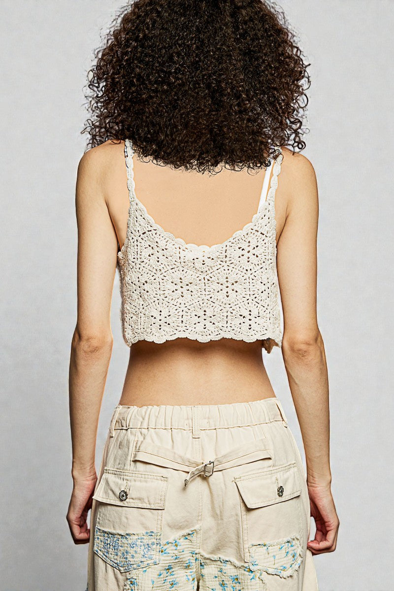 Person wearing a white crochet tank top and beige pants against a plain background