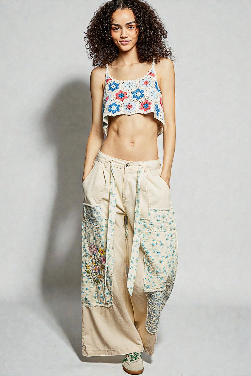 Woman wearing a floral crop top and beige pants with embroidery on a plain background