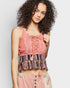 Woman wearing a colorful sleeveless top with lace-up front and fringes on a plain background
