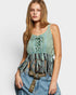Woman wearing a green lace-up top with fringe details and blue jeans on a white background