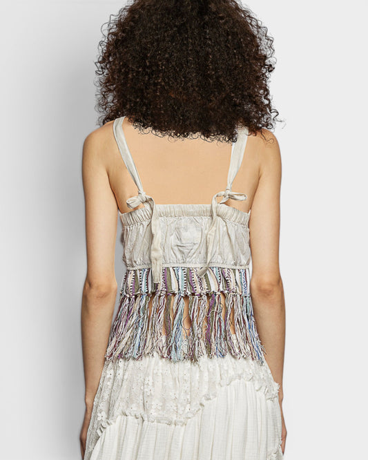 Person wearing a white dress with colorful fringe details on a plain background