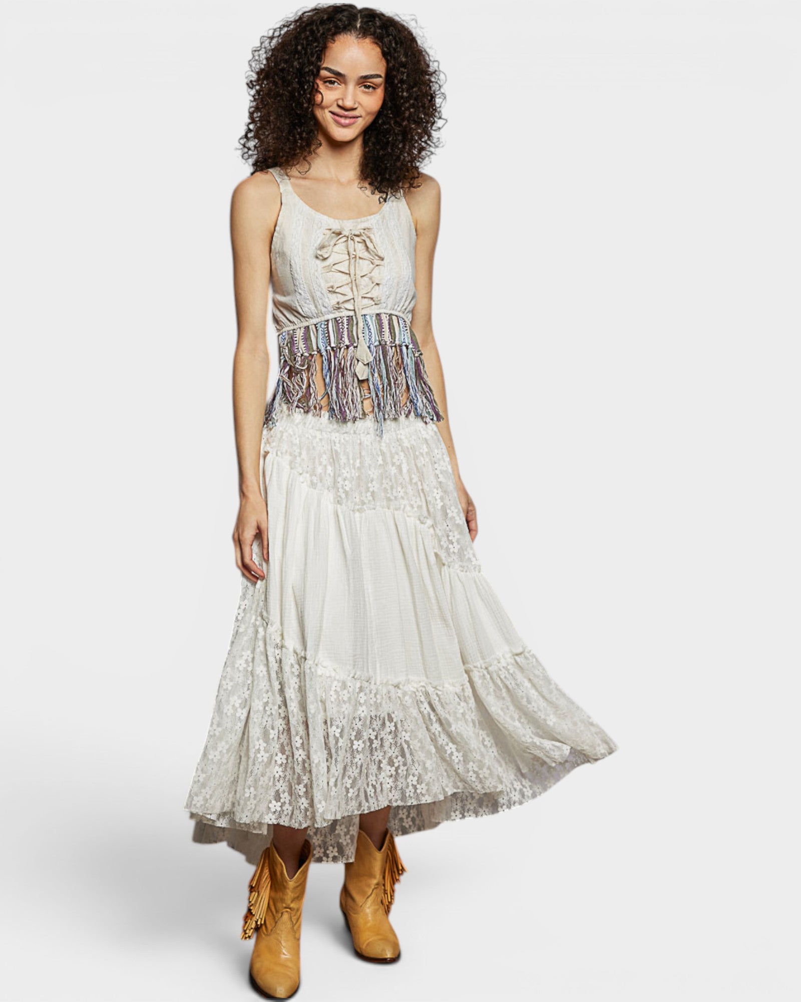 Woman wearing a white lace dress with a patterned belt and yellow boots on a white background