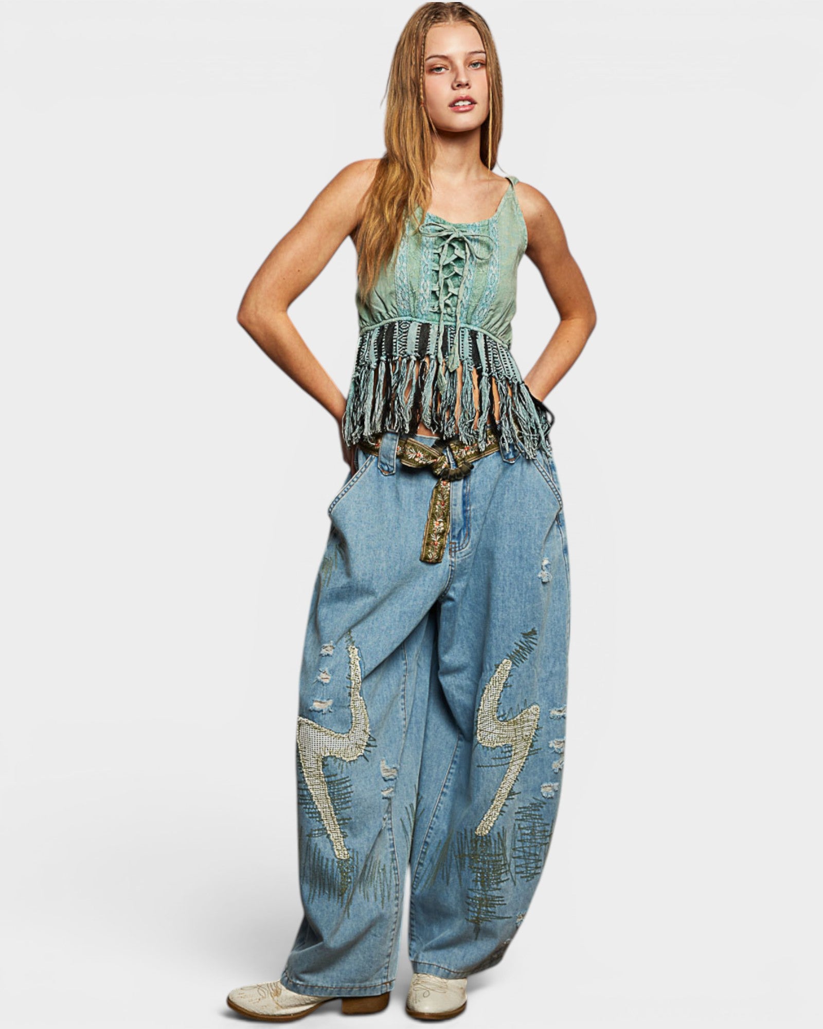 Woman wearing a sleeveless top and denim pants with decorative elements on a white background