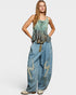 Woman wearing a sleeveless top and denim pants with decorative elements on a white background