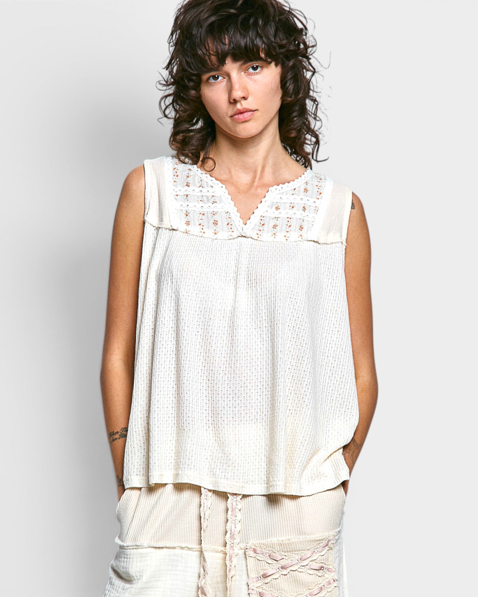 Woman wearing a white sleeveless top with lace details against a plain background