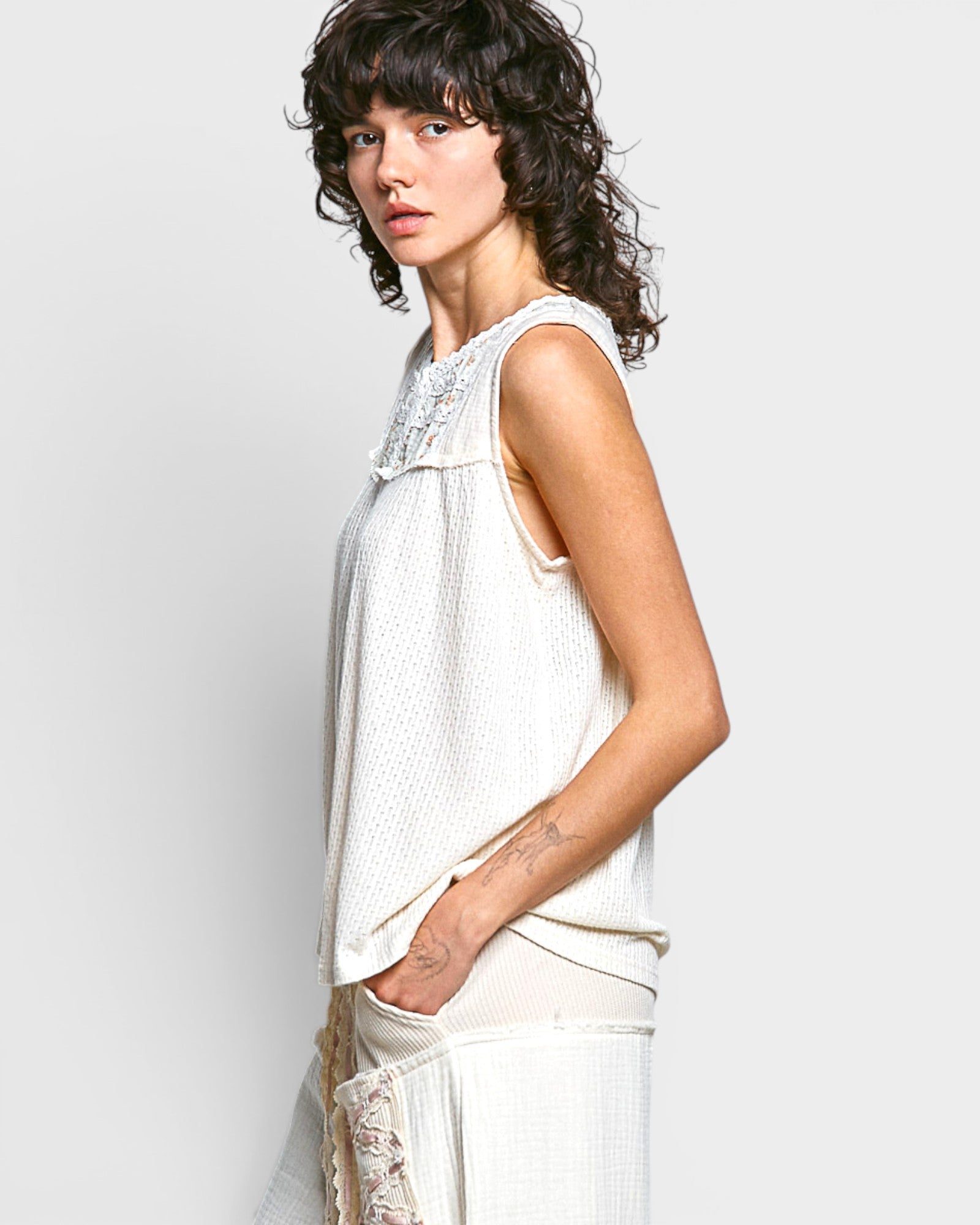 Woman wearing a white sleeveless top with lace details on a light gray background
