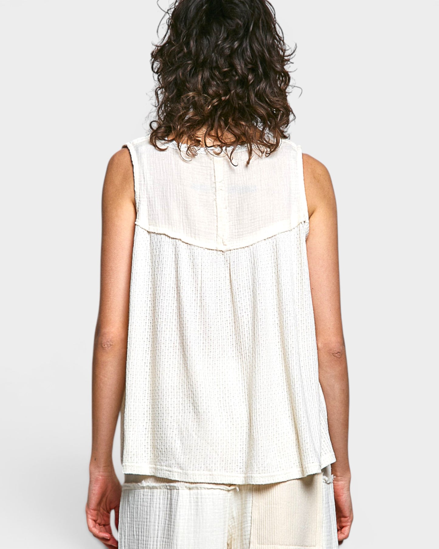 Person wearing a white sleeveless top on a plain background