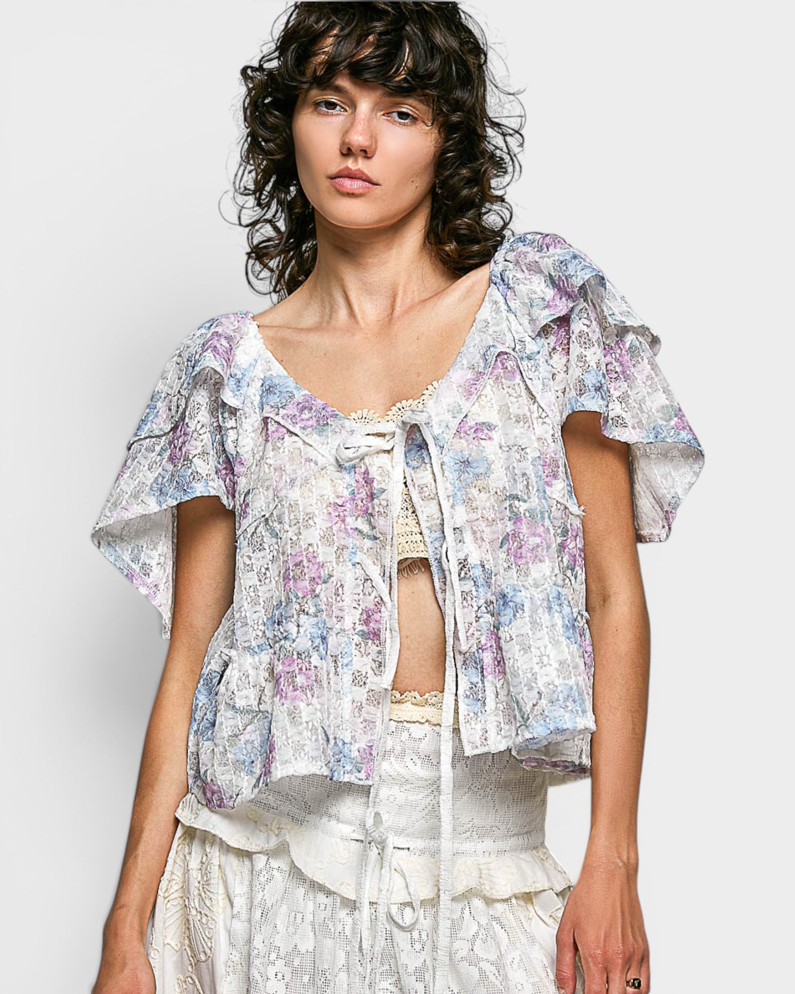 Woman wearing a floral blouse with ruffled sleeves on a plain background