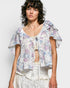 Woman wearing a floral blouse with ruffled sleeves on a plain background