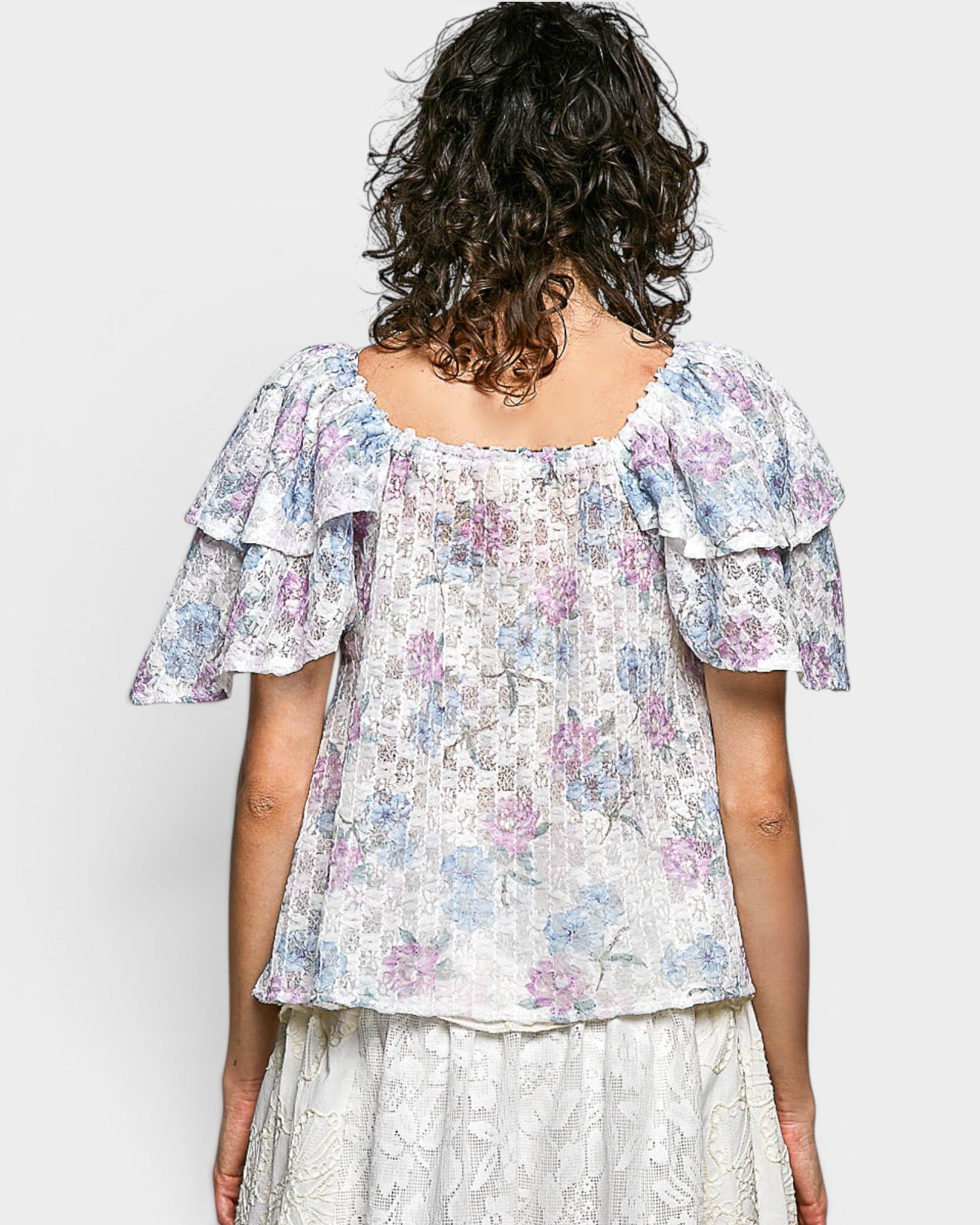 Woman wearing a floral blouse with ruffled sleeves on a plain background