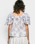 Woman wearing a floral blouse with ruffled sleeves on a plain background