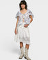 Woman wearing a floral top and white lace skirt with cowboy boots on a plain background