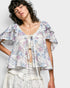 Woman wearing a floral blouse with ruffled sleeves against a plain background