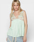 Woman wearing a light green sleeveless top with floral lace details on a white background