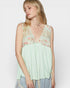 Woman wearing a light green sleeveless top with floral lace details on a white background