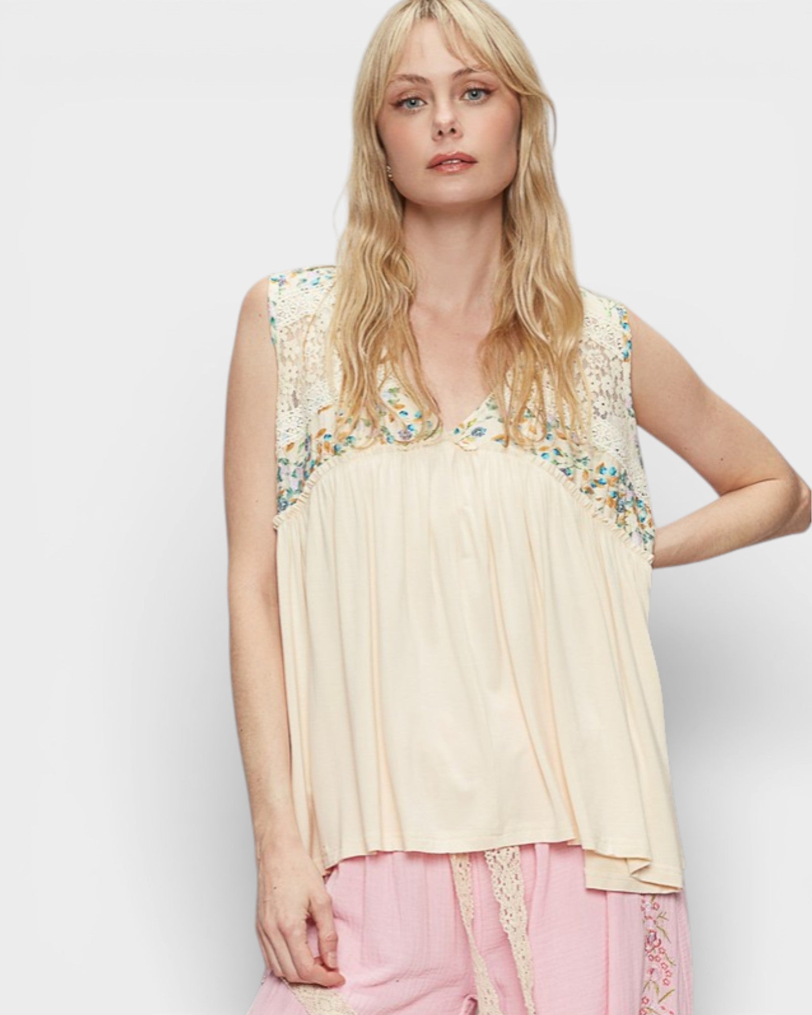 Woman wearing a beige sleeveless top with floral embroidery on a white background