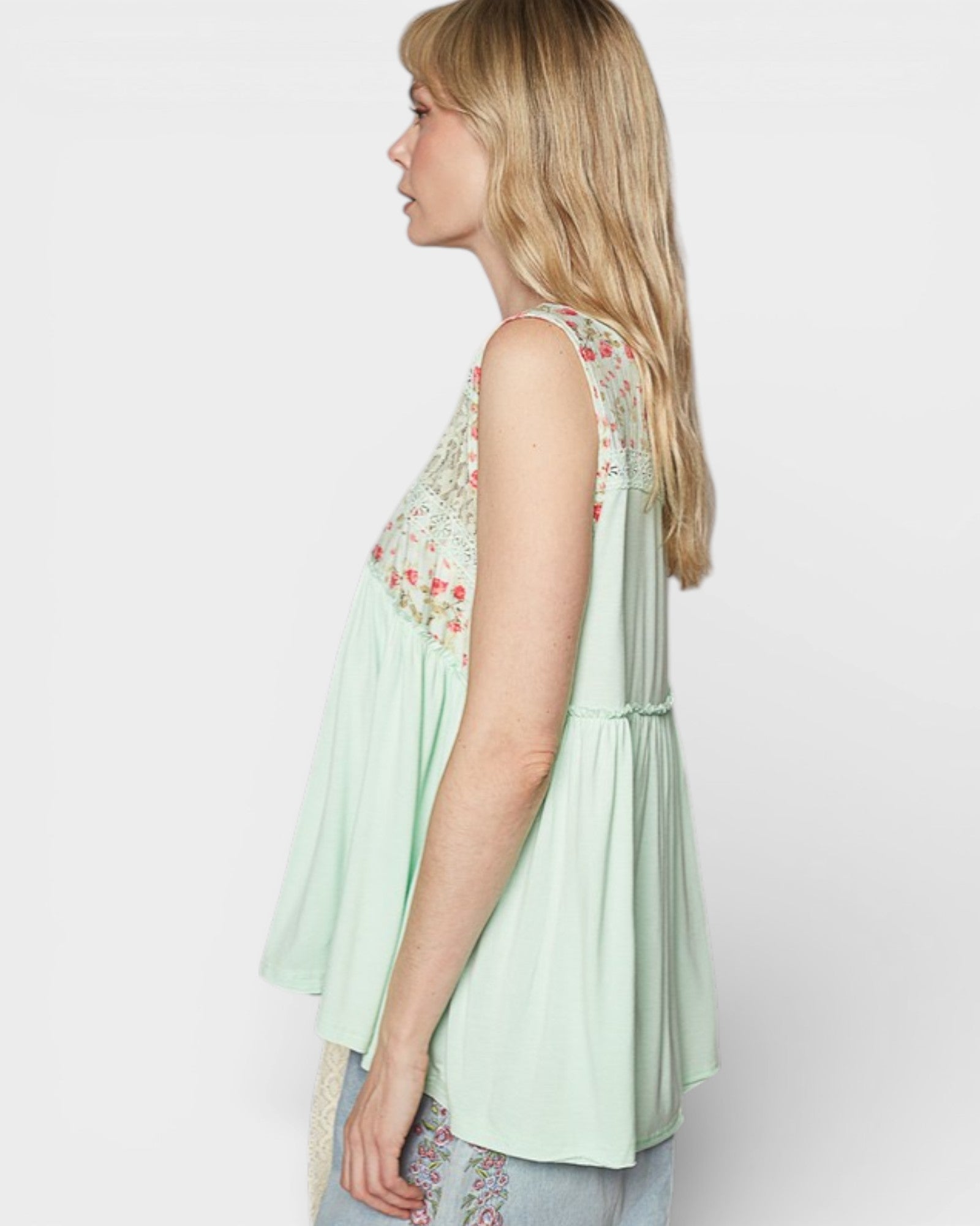 Woman wearing a light green sleeveless top with floral embroidery on a white background