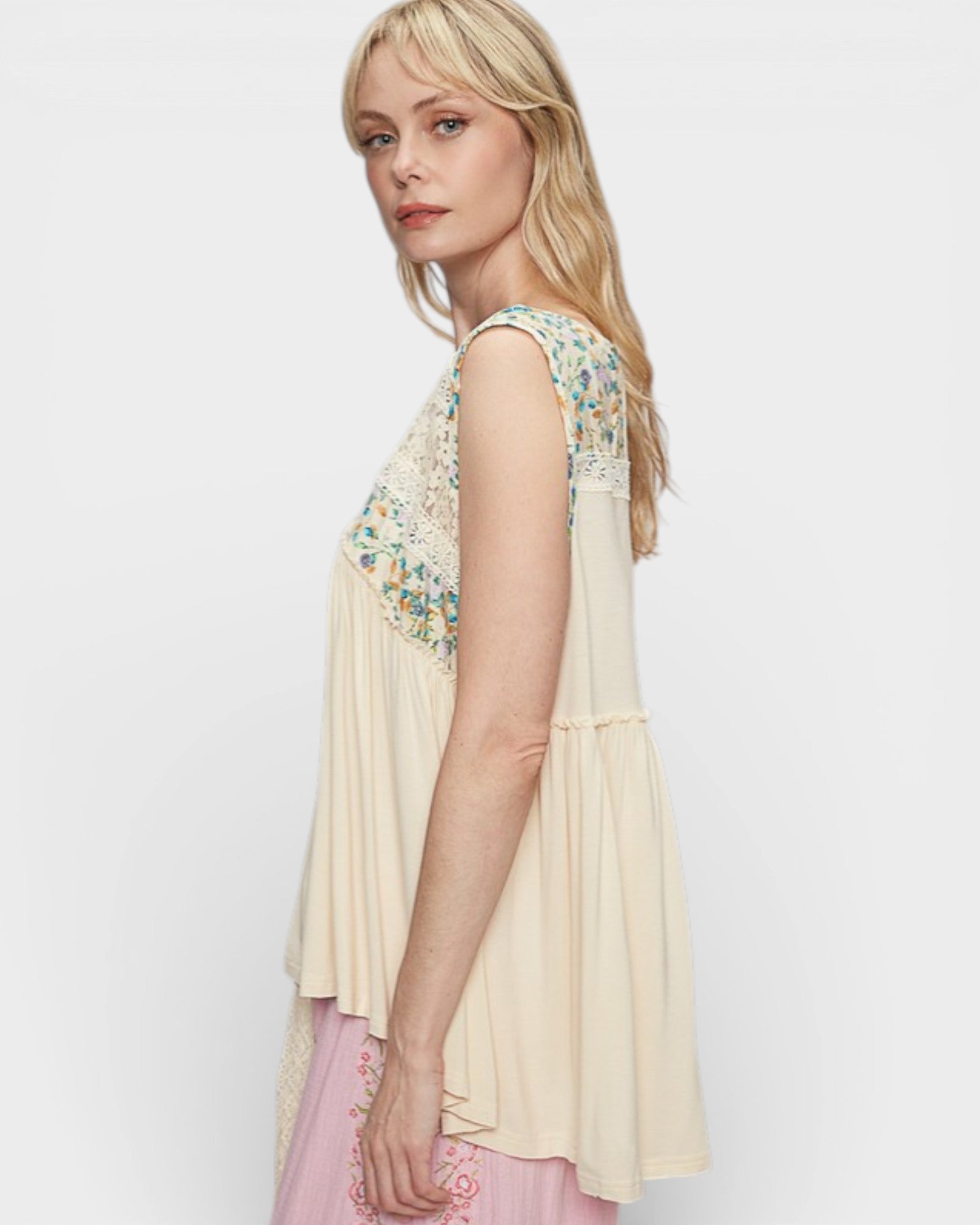 Woman wearing a beige sleeveless top with floral embroidery on a white background