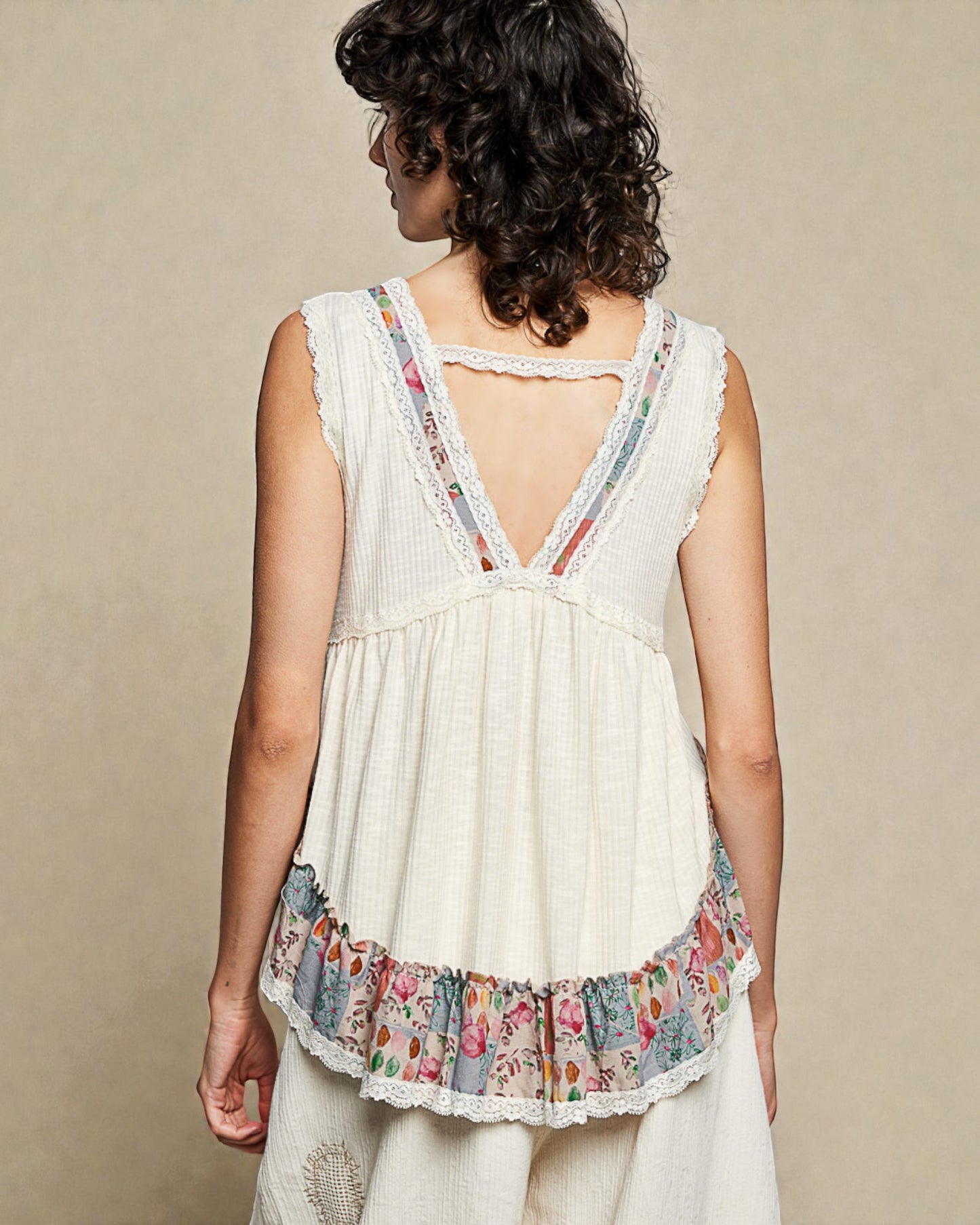Woman wearing a white sleeveless top with floral trim on a beige background