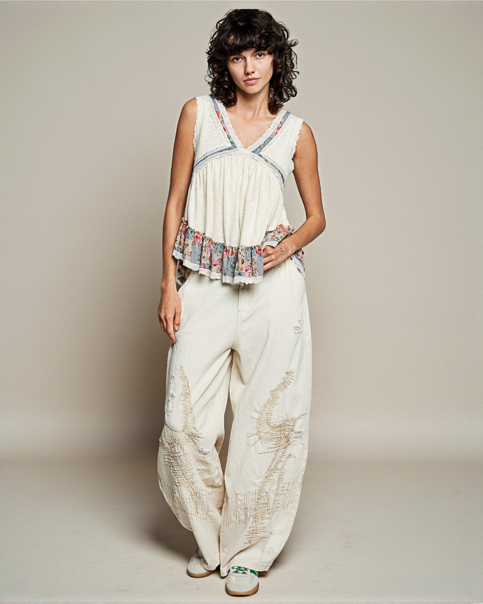 Woman wearing a white sleeveless top with floral details and wide-leg pants on a plain background