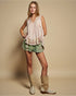 Woman wearing a sleeveless top and shorts with boots on a beige background