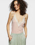 Woman wearing a pink lace-trimmed top with green pants on a white background