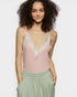 Woman wearing a pink lace camisole and green pants on a plain background