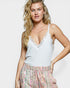 Woman wearing a white lace camisole and patterned pants on a plain background